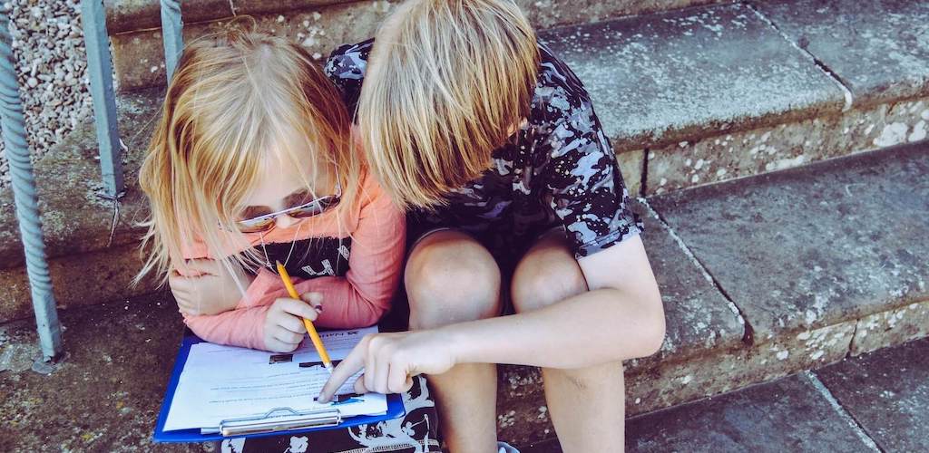 Two children on steps with a clipboard trying to figure something out together.